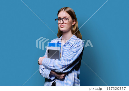 Portrait female college student holding textbooks tablet on blue background 117320557
