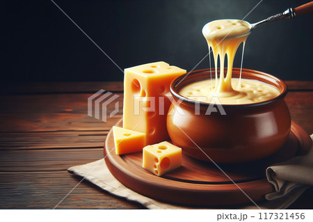 Melted cheese pot, spoon lifting gooey texture. Beside, holed cheese block, likely Swiss. On wooden table against dark background, fondue scene 117321456