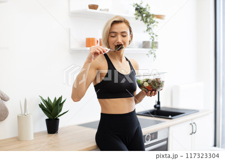 Fit woman enjoying healthy salad in modern kitchen 117323304