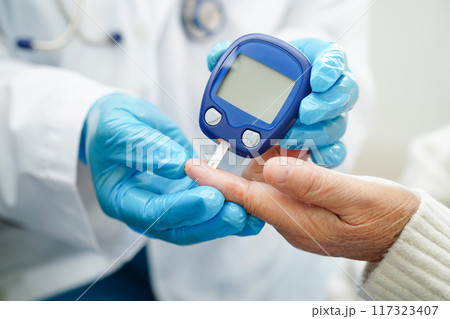 Asian doctor using digital glucose meter for check sample blood sugar level to treatment diabetes. 117323407