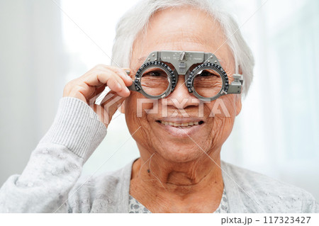 Asian senior woman wearing ophthalmic vision eye test and using optical trial frame. Asian senior woman wearing ophthalmic vision eye test and using optical trial frame. 117323427