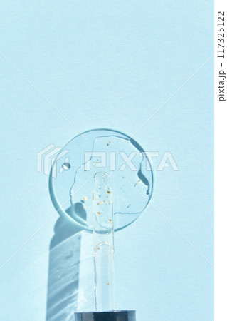 Serum gel texture swatch. Transparent drop with golden sparkles. Blue background 117325122