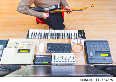 top view of male musician playing electric guitar in home studio, showing professional audio recording equipment and computer on desk 117325270