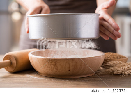 Sifting flour through sieve into wooden bowl, Food ingredient prepare for cooking or baking 117325734