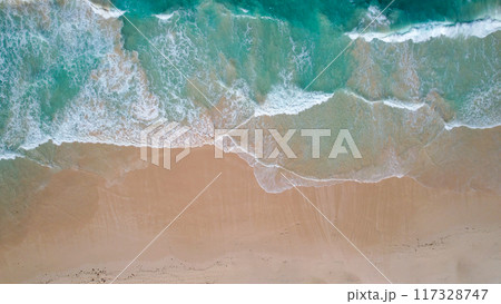 Aerial view of turquoise waves gently crashing onto a sandy beach. The oceans clear water, mixed with white foam, creates a tranquil Aerial view of turquoise waves gently crashing onto a sandy beach. The oceans clear water, mixed with white foam, creates a tranquil 117328747