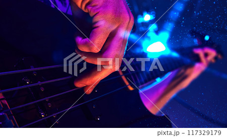 Close-up of musician's hand playing electric guitar, illuminated by vibrant blue and purple stage lights, capturing intensity of live performance. Close-up of musician's hand playing electric guitar, illuminated by vibrant blue and purple stage lights, capturing intensity of live performance. 117329179