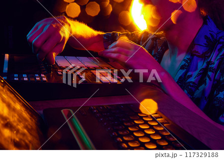 DJ's hands work mixer, bathed in ambient glow of stage lights, shaping rhythm that will move crowd. DJ's hands work mixer, bathed in ambient glow of stage lights, shaping rhythm that will move crowd. 117329188
