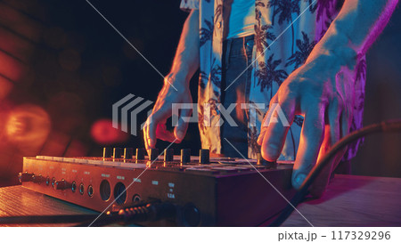 Hands on mixer, bathed in warm neon light, setting stage for night of beats and rhythm, where music becomes pulse of crowd. Hands on mixer, bathed in warm neon light, setting stage for night of beats and rhythm, where music becomes pulse of crowd. 117329296