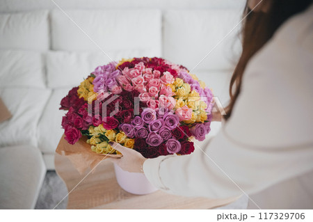 Person arranging a vibrant bouquet of roses indoors, surrounded by a cozy living room setting 117329706