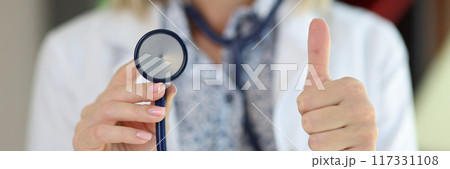 Physician posing in clinic office with stethoscope and showing thumb-up sign 117331108