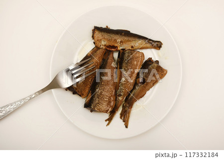 Sprats on a white plate with a fork. Canned fish in oil. Fish appetizer. 117332184