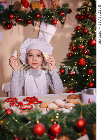 A cheerful girl in a chef's hat shows Christmas gingerbread cookies in the shape of a Christmas tree. 117332258