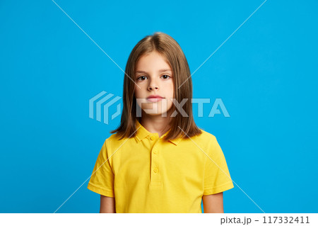 Portrait of young 9 years old girl with brown hair, in pink polo shirt looking at camera with calm face, posing against blue studio background Portrait of young 9 years old girl with brown hair, in pink polo shirt looking at camera with calm face, posing against blue studio background 117332411