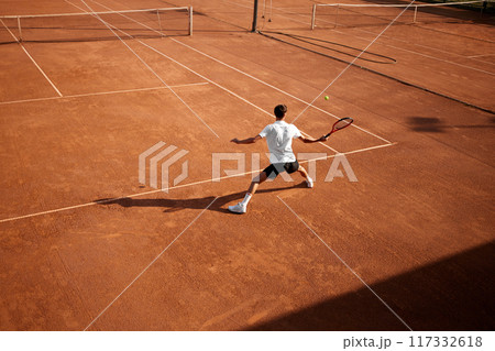 Endurance and motivation. Focused man, tennis player in motion on clay court, receiving the ball, playing on open air arena. Endurance and motivation. Focused man, tennis player in motion on clay court, receiving the ball, playing on open air arena. 117332618