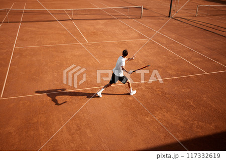 Intense focus of young competitive man, tennis player in motion on clay court with racket, training, preparing for upcoming championship game. Intense focus of young competitive man, tennis player in motion on clay court with racket, training, preparing for upcoming championship game. 117332619