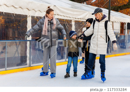 Young adult attractive beautiful caucasian woman enjoy having fun with little toddler son at outdoor skating rink while travel in old european city in winter. Mom and child holiday sport acitivitie Young adult attractive beautiful caucasian woman enjoy having fun with little toddler son at outdoor skating rink while travel in old european city in winter. Mom and child holiday sport acitivitie 117333284