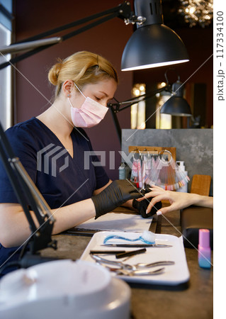 Manicurist in protective facial mask and gloves providing safety manicure Manicurist in protective facial mask and gloves providing safety manicure 117334100