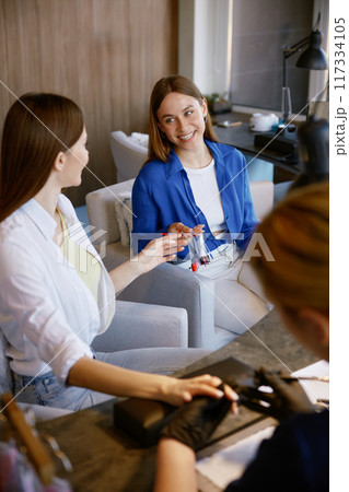 Young woman advising friend color of nail polish in spa salon 117334105