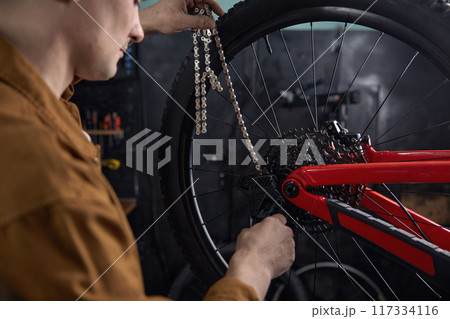 Man mechanic performing mountain bike maintenance fixing chain Man mechanic performing mountain bike maintenance fixing chain 117334116