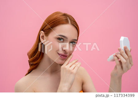 Ginger woman with bare shoulders with cream powder in hands 117334399