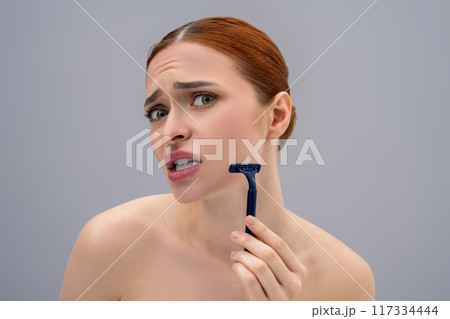 Young woman holding a shaver in hands and looking scared Young woman holding a shaver in hands and looking scared 117334444