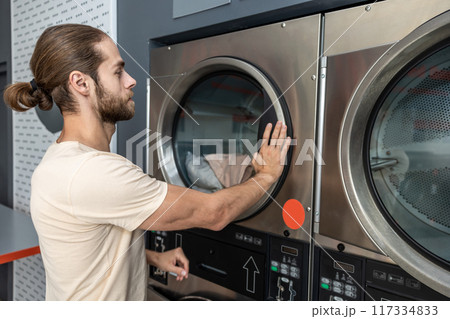 Man doing household chores washing clothing at industrial laundromat Man doing household chores washing clothing at industrial laundromat 117334833