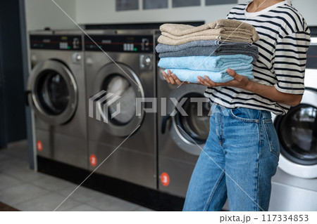 Unrecognizable woman carrying stack of towels at public laundromat Unrecognizable woman carrying stack of towels at public laundromat 117334853