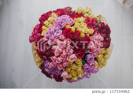 A vibrant arrangement of colorful roses on a wooden table in a bright room 117334962