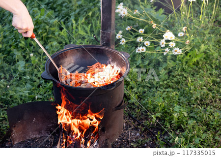 stir chopped carrots in a cast iron cauldron over a fire to prepare pilaf while frying outdoors stir chopped carrots in a cast iron cauldron over a fire to prepare pilaf while frying outdoors 117335015