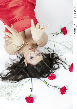 Curvy girl posing with a red dress and some red flowers around her Curvy girl posing with a red dress and some red flowers around her 117335937