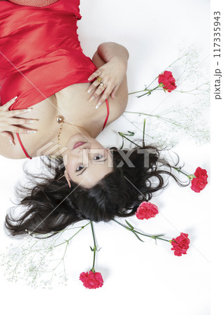 Curvy girl posing with a red dress and some red flowers around her Curvy girl posing with a red dress and some red flowers around her 117335943