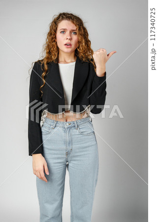Smiling Young Woman Pointing While Posing in a Studio 117340725