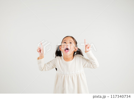 Asian happy portrait cute young kid girl makes gesture fingers point upwards above presenting product something, studio shot isolated on white background, kindergarten children woman smile 117340734