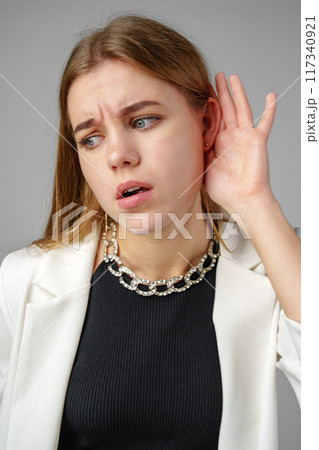Woman in White Jacket Listening With Hand to Ear 117340921
