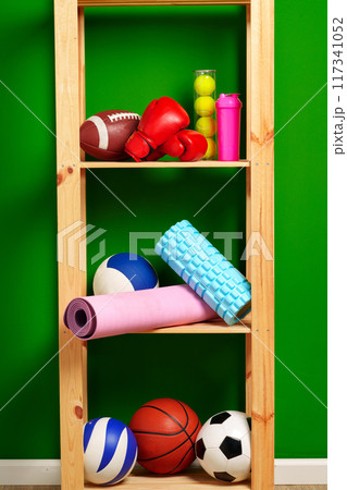 Shelves with different sports equipment against green wall 117341052