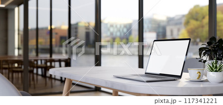 A laptop on a table by the window with a city view, in a contemporary office co-working space. A laptop on a table by the window with a city view, in a contemporary office co-working space. 117341221