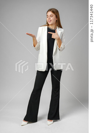 Confident Young Businesswoman Presenting With Hand Gesture in Studio Setting Confident Young Businesswoman Presenting With Hand Gesture in Studio Setting 117341440