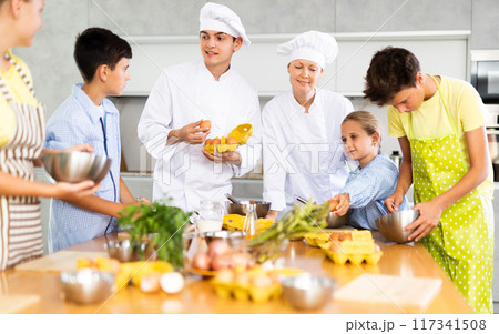 Young guy and adult woman cook teaches group of children to cook Young guy and adult woman cook teaches group of children to cook 117341508