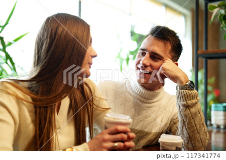 Smiling Couple Enjoying Warm Beverages at a Cozy Cafe on a Sunny Afternoon Smiling Couple Enjoying Warm Beverages at a Cozy Cafe on a Sunny Afternoon 117341774