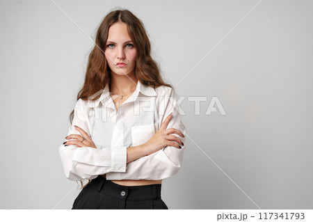 A woman is standing wearing a white shirt and black pants. She has a confident stance and is looking directly at the camera. A woman is standing wearing a white shirt and black pants. She has a confident stance and is looking directly at the camera. 117341793