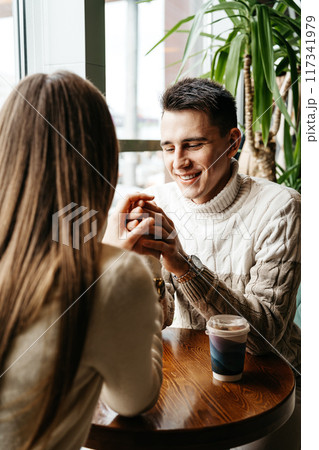 Smiling Man Engaged in a Casual Conversation at a Cozy Cafe During Daytime Smiling Man Engaged in a Casual Conversation at a Cozy Cafe During Daytime 117341979
