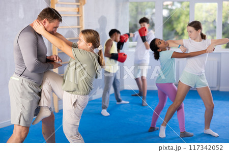 Tween girl performing knee strike in midsection to instructor in self-defense sparring Tween girl performing knee strike in midsection to instructor in self-defense sparring 117342052