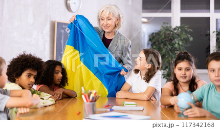 Female teacher showing ukrainian flag to kids in geography class 117342168