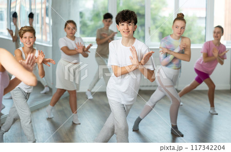 Male boy student repeats movements of unrecognizable teacher during group modern dance class. 117342204