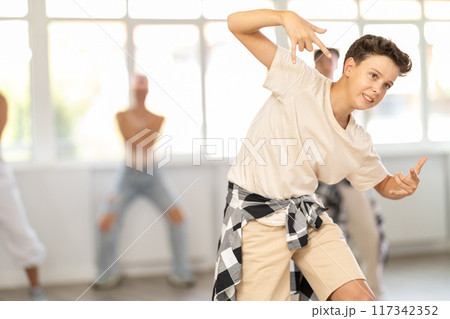 Group of sporty teenagers practicing hip hop dance in training hall during dancing classes Group of sporty teenagers practicing hip hop dance in training hall during dancing classes 117342352