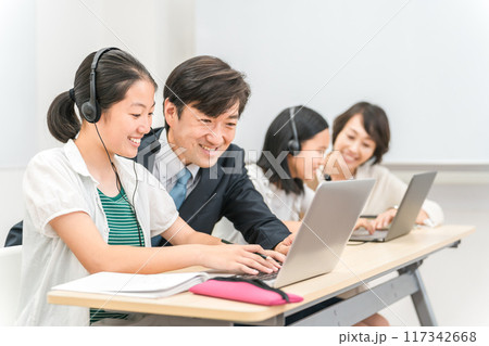 塾・学校の教室でパソコンとヘッドセットを使って先生に勉強を教わる小学生・中学生・高校生の子供 117342668