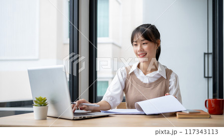 An Asian businesswoman is working at her desk, reviewing business report and working on her laptop. 117343113
