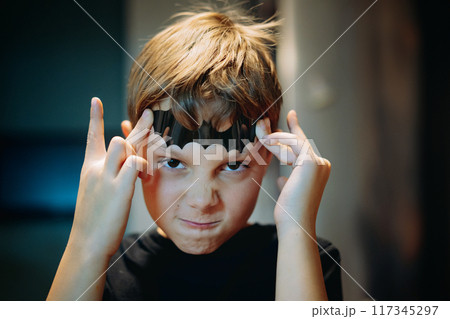cute caucasian boy holding a paper bat shape on his forehead making scary face. 117345297