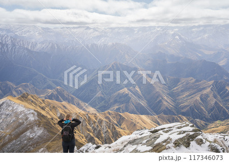Female hiker standing on top of the mountain enjoying views on mountain ranges in front of her Female hiker standing on top of the mountain enjoying views on mountain ranges in front of her 117346073