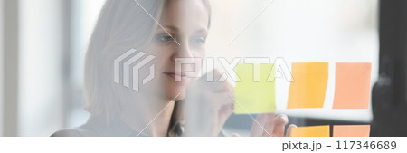 Manager putting stickers note on transparent glass wall in office Manager putting stickers note on transparent glass wall in office 117346689
